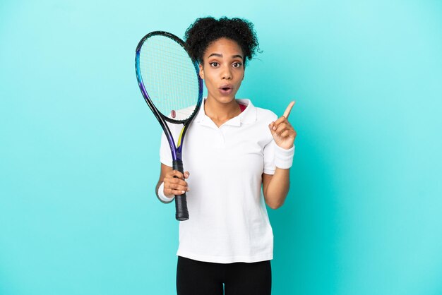 Jeune femme de joueur de tennis isolée sur fond bleu dans l'intention de réaliser la solution tout en levant un doigt vers le haut