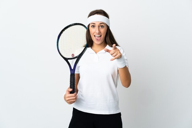 Jeune femme joueur de tennis sur mur blanc isolé surpris et pointant vers l'avant