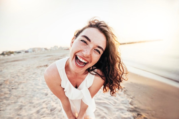 Jeune femme joyeuse en chemise blanche souriant à la caméra sur la plage