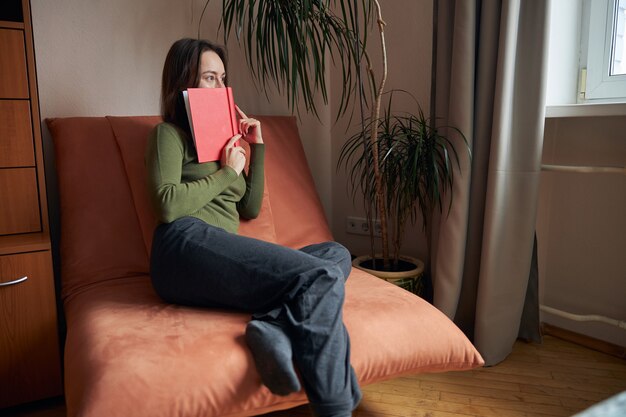 Une jeune femme joyeuse, confiante et heureuse se détend dans son fauteuil confortable à la maison avec des livres