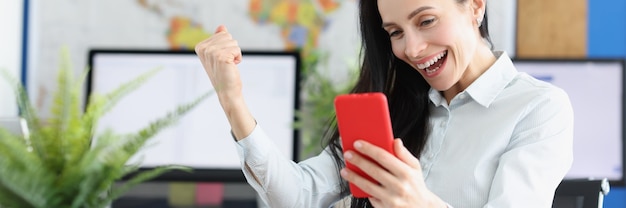 Une jeune femme joyeuse dans l'euphorie regarde l'écran du smartphone