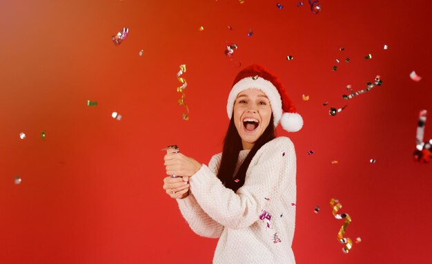 Photo une jeune femme joyeuse debout sur un fond rouge tandis que des confettis tombent sur elle.