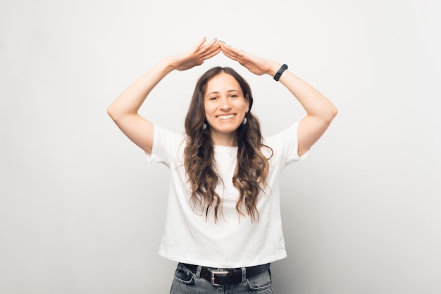 Une jeune femme joyeuse fait le geste du toit sur fond blanc.