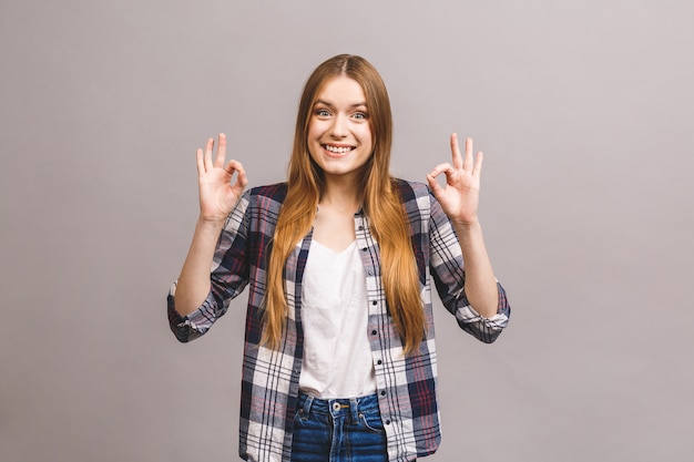 Jeune femme joyeuse heureuse montrant signe ok isolé contre le mur gris.