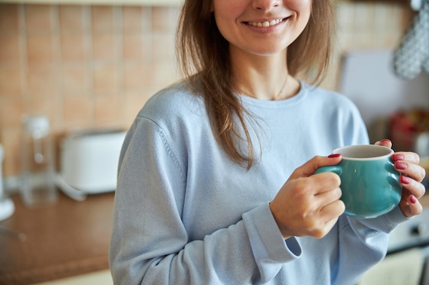 Une jeune femme joyeuse et heureuse prépare un thé savoureux dans sa cuisine à la maison