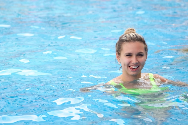 Une jeune femme joyeuse en maillot de bain vert clair se baigne dans la piscine