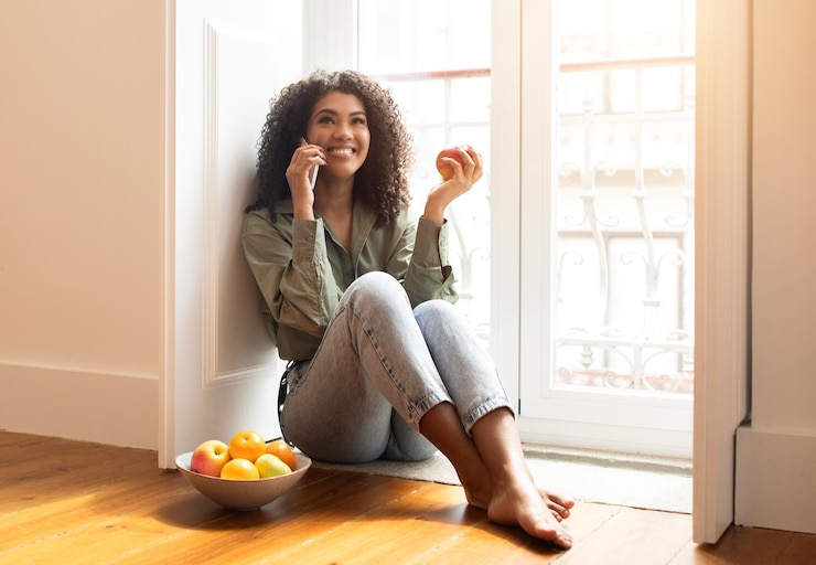 Photo jeune femme joyeuse parlant sur un smartphone, assise et communiquant depuis la maison