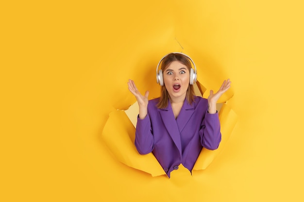 Une jeune femme joyeuse pose sur un fond de trou de papier jaune déchiré, émotionnel et expressif