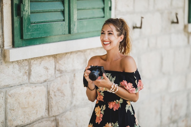 Jeune femme joyeuse prenant des photos avec son appareil photo numérique tout en explorant une ville méditerranéenne.