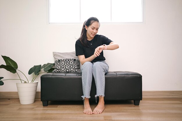 Une jeune femme joyeuse regardant une montre assise sur un banc à la maison.