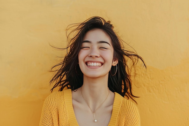 Une jeune femme joyeuse souriante avec les cheveux soufflant dans le vent contre un mur de texture jaune