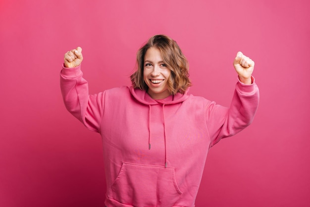 Une jeune femme joyeuse tient les deux mains tout en souriant à la caméra et en célébrant