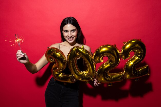 Une jeune femme joyeuse vêtue d'une robe noire tient les chiffres 2022 et des cierges magiques.