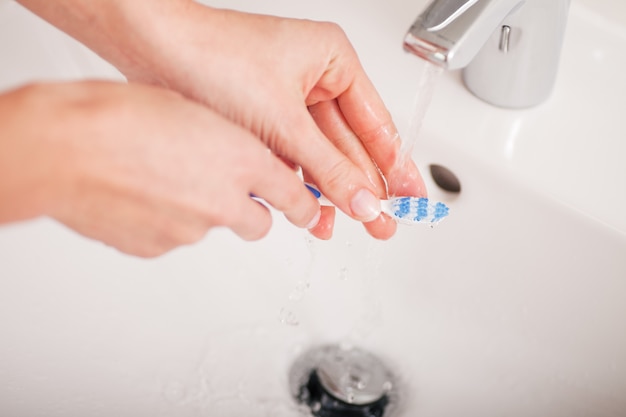 Jeune femme (juste les mains) nettoyant sa brosse à dents