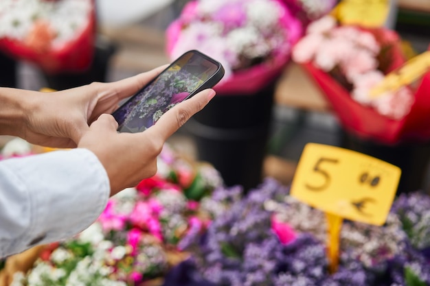 Jeune femme latina capturant la beauté vibrante des fleurs à l'étal d'un vendeur de rue avec son téléphone