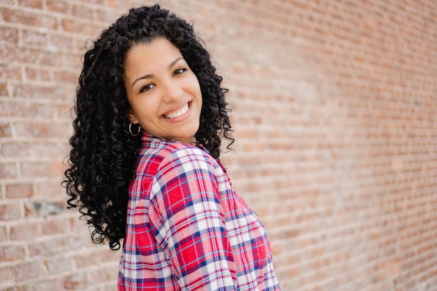 Jeune femme latina étudiante en échange avec des boucles regarde l'espace de copie de fond de brique de caméra