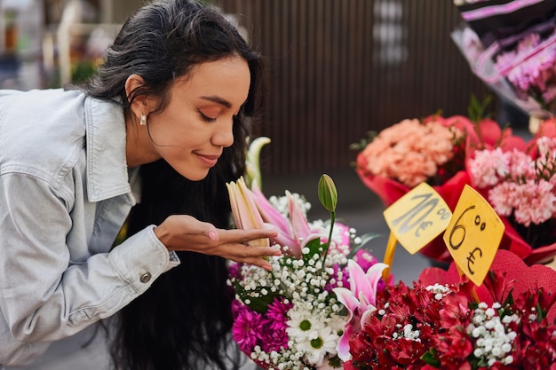 Jeune femme Latina se délectant de la beauté parfumée des fleurs colorées à l'étal d'un vendeur de rue