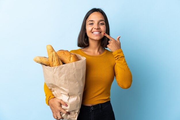 Jeune femme latine l'achat de pains isolés sur bleu donnant un geste de pouce en l'air