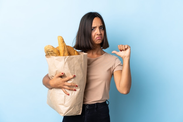 Jeune femme latine l'achat de pains isolés sur bleu fier et satisfait de soi