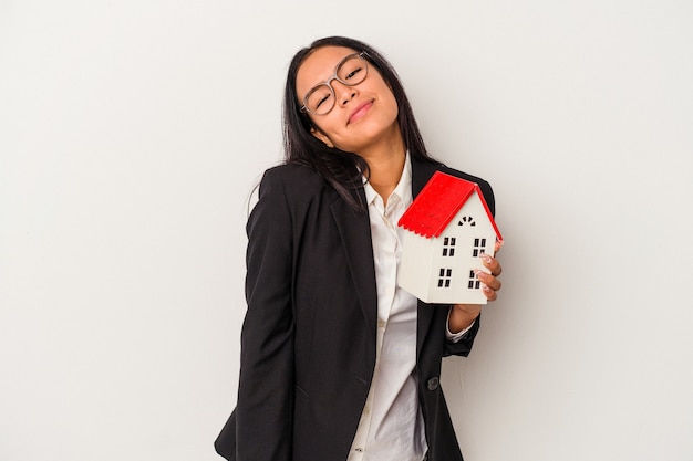 Jeune femme latine d'affaires tenant une maison de jouet isolée sur fond blanc rêvant d'atteindre des objectifs et des buts