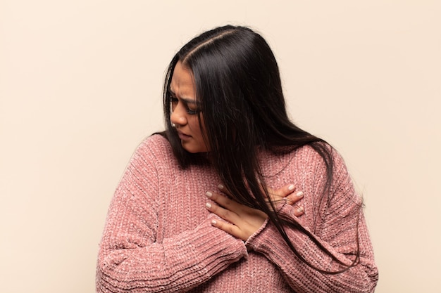 Jeune femme latine à l'air triste, blessée et navrée, tenant les deux mains près du cœur, pleurant et se sentant déprimée