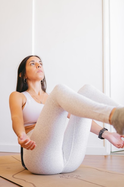 Photo une jeune femme latine assise sur son tapis de yoga en équilibre avec ses jambes et ses bras levés à la maison