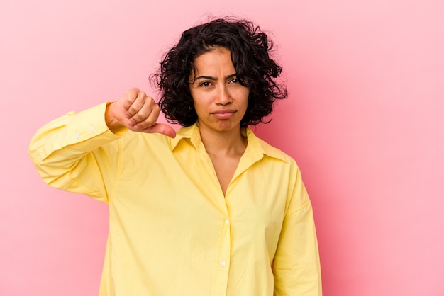 Jeune femme latine bouclée isolée sur fond rose montrant un geste d'aversion, les pouces vers le bas. Notion de désaccord.