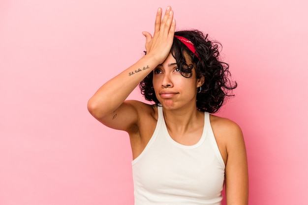 Jeune femme latine bouclée isolée sur fond rose oubliant quelque chose, frappant le front avec la paume et fermant les yeux.