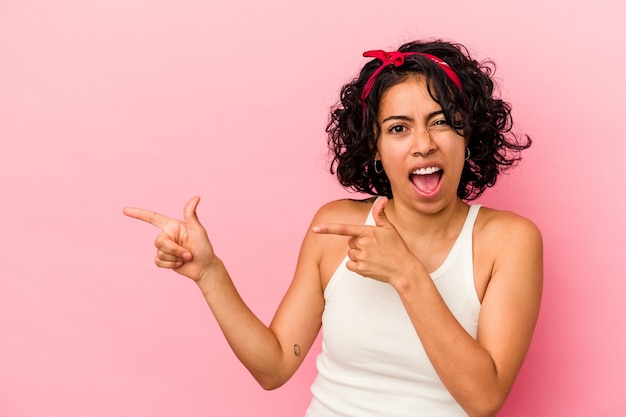 Jeune femme latine bouclée isolée sur fond rose pointant avec les index vers un espace de copie, exprimant l'excitation et le désir.