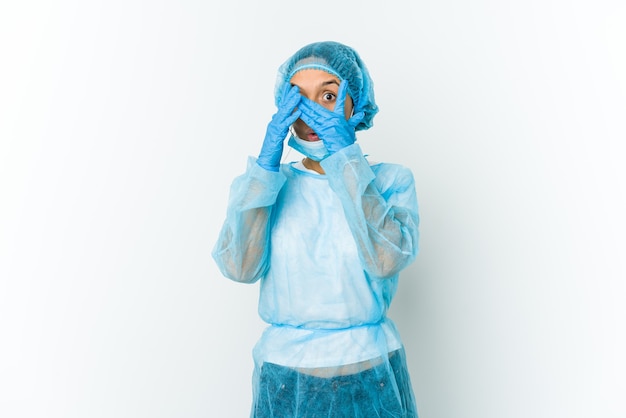 Jeune femme latine de chirurgien isolée sur fond blanc clignote à travers les doigts effrayés et nerveux.