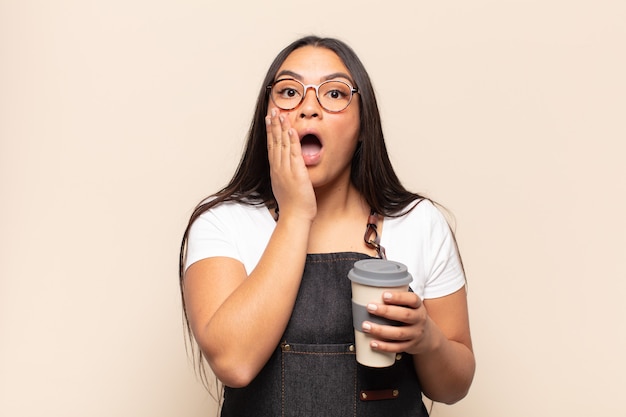 Jeune femme latine choquée et effrayée, à la terrifiée avec la bouche ouverte et les mains sur les joues