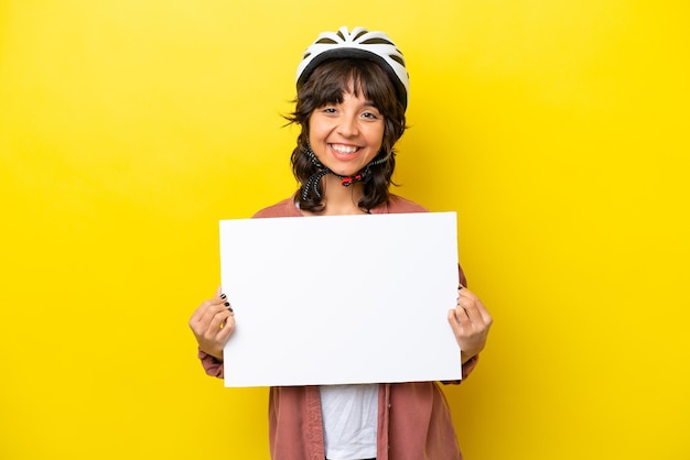 Jeune femme latine cycliste isolée sur fond jaune tenant une pancarte vide avec une expression heureuse