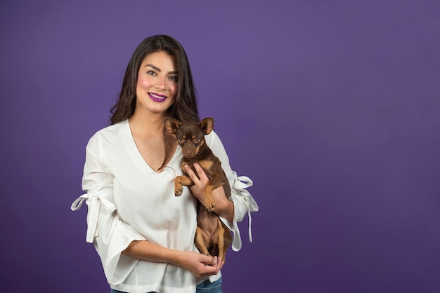 Jeune femme latine embrasse son chien chihuahua sur fond violet isolé