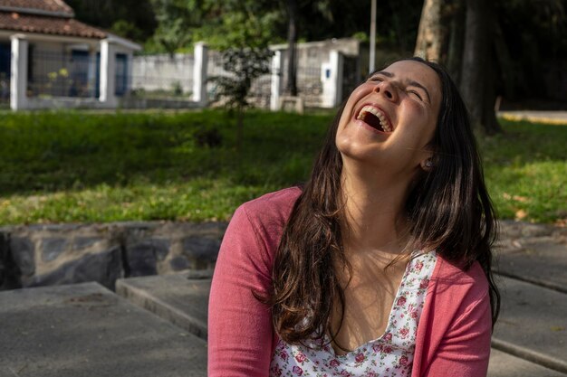 Jeune femme latine est heureuse et souriante pour l'arrivée du printemps, elle est assise dans le parc
