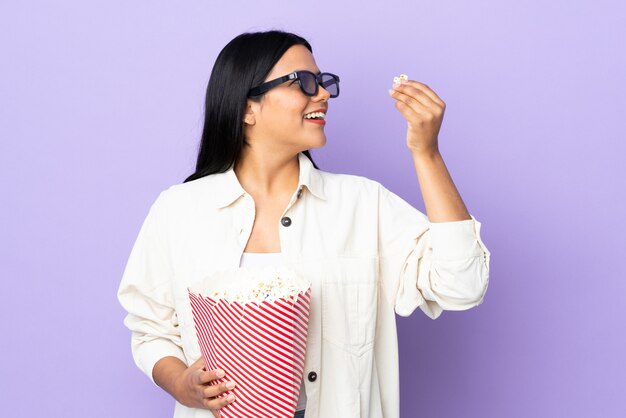 Jeune femme latine femme sur mur blanc avec des lunettes 3d et tenant un grand seau de pop-corn