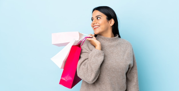 Jeune femme latine femme sur mur bleu tenant des sacs à provisions et regardant en arrière