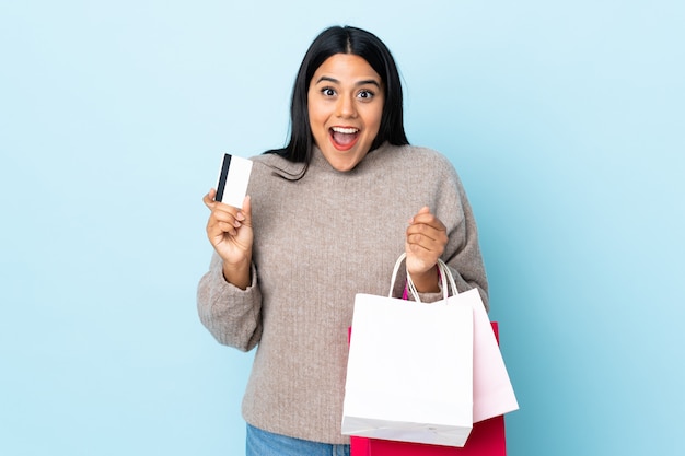 Jeune femme latine femme sur mur bleu tenant des sacs à provisions et surpris