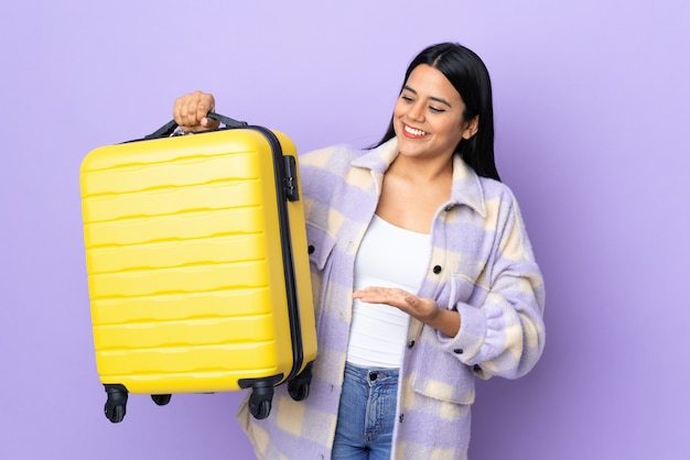 Jeune femme latine femme sur mur violet en vacances avec valise de voyage