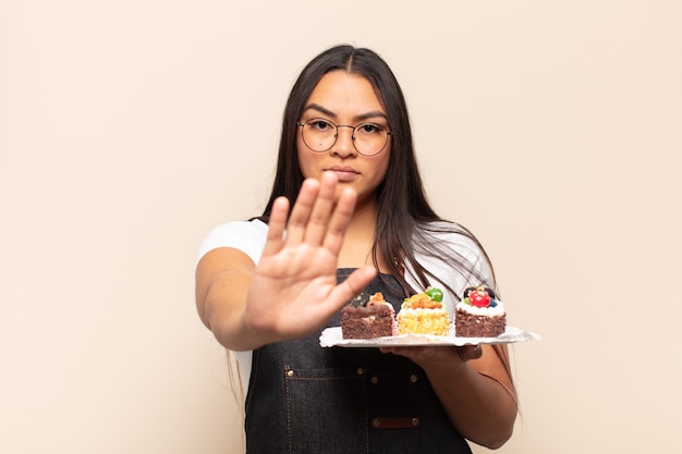 Photo jeune femme latine à la grave, sévère, mécontent et en colère montrant la paume ouverte faisant le geste d'arrêt