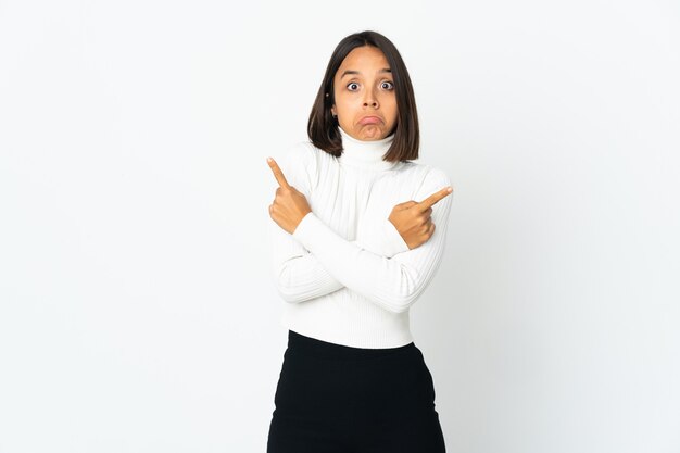 Jeune femme latine isolée sur fond blanc pointant vers les latéraux ayant des doutes