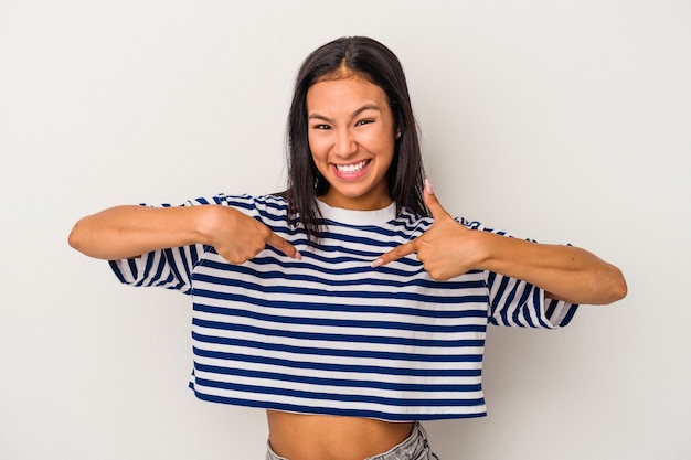 Jeune femme latine isolée sur fond blanc surprise en pointant du doigt, souriant largement.