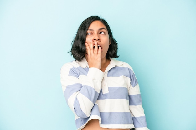 Jeune femme latine isolée sur fond bleu bâillant montrant un geste fatigué couvrant la bouche avec la main.