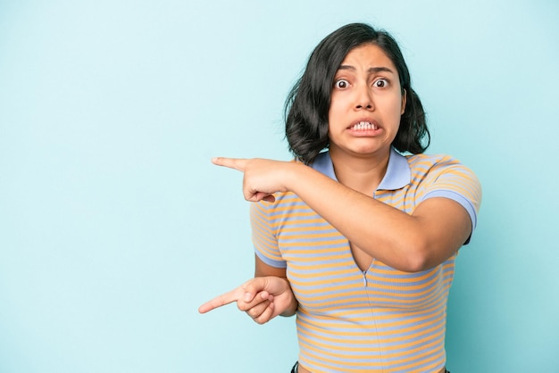 Jeune femme latine isolée sur fond bleu choquée pointant avec l'index vers un espace de copie.