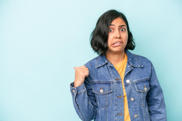 Jeune femme latine isolée sur fond bleu choquée pointant avec l'index vers un espace de copie.