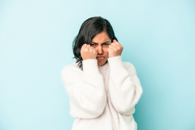 Jeune femme latine isolée sur fond bleu jetant un coup de poing, colère, combat à cause d'une dispute, boxe.