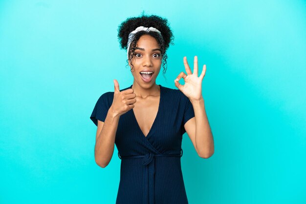 Jeune femme latine isolée sur fond bleu montrant un signe ok et un geste du pouce vers le haut