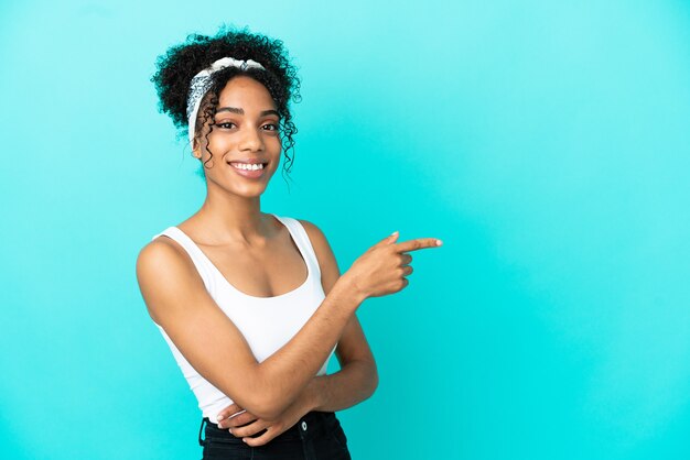 Jeune femme latine isolée sur fond bleu, pointant le doigt sur le côté