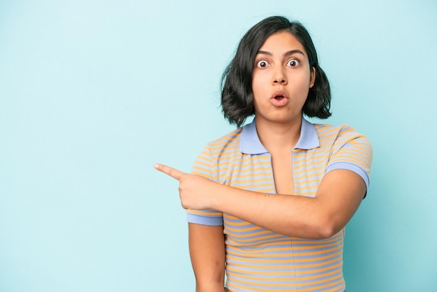 Jeune femme latine isolée sur fond bleu pointant vers le côté