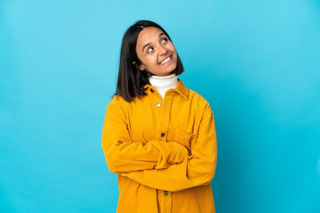 Jeune femme latine isolée sur fond bleu regardant en souriant