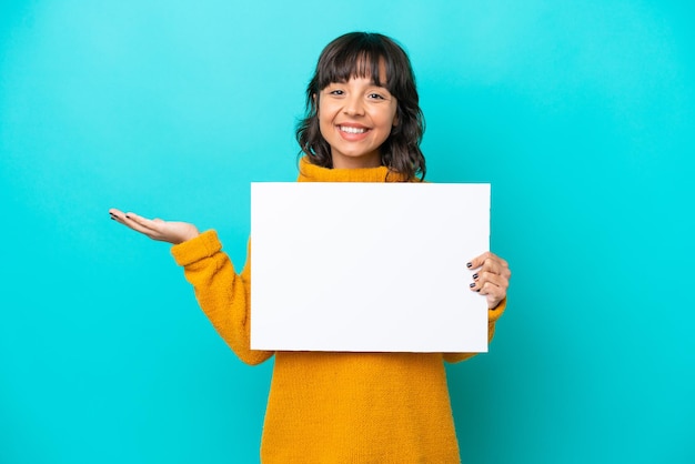 Jeune femme latine isolée sur fond bleu tenant une pancarte vide avec une expression surprise